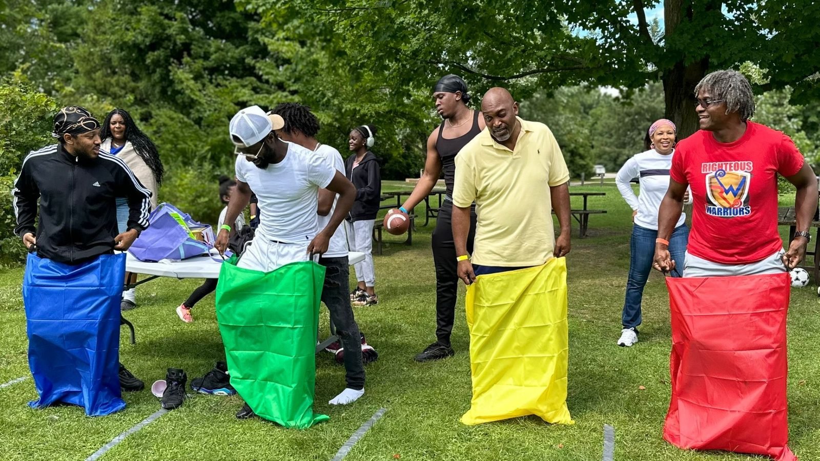 Brethren taking part in a sack race at an outdoor gathering.