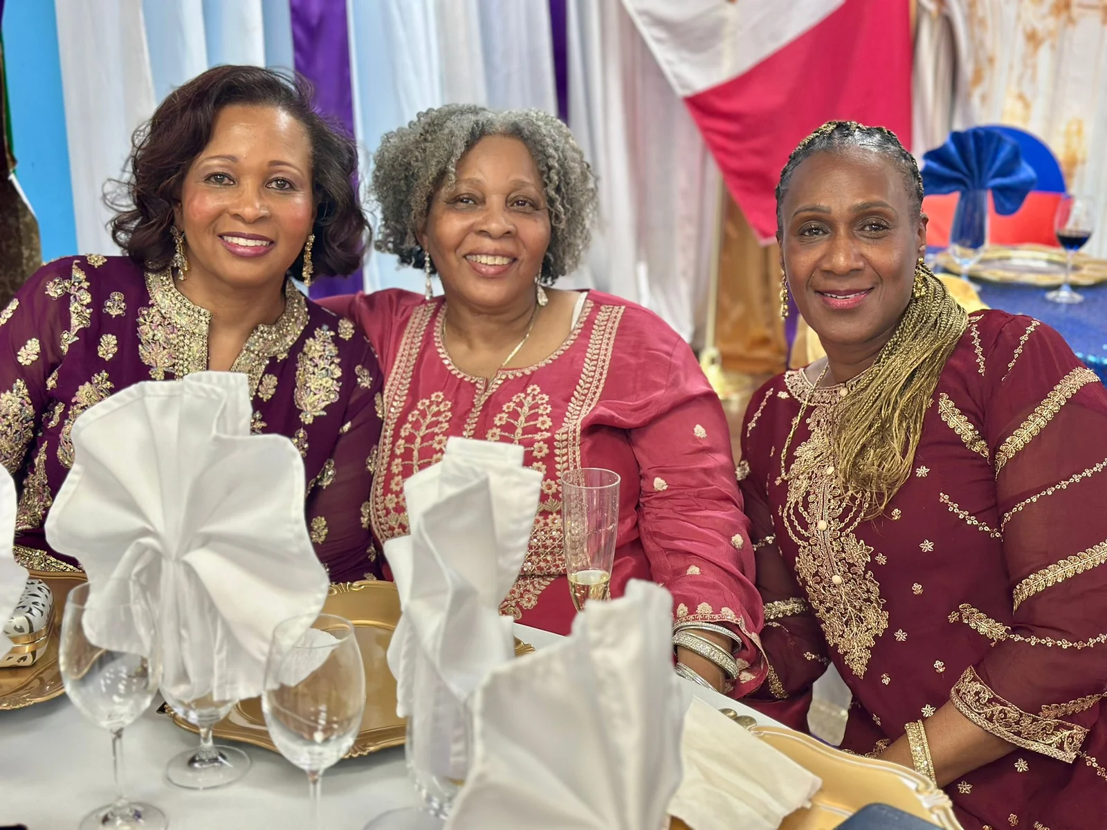 Three women smiling together at a decorated feast table.